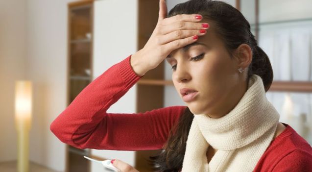 אישה עם חום, מחזיקה מדחום, נראית מודאגת.