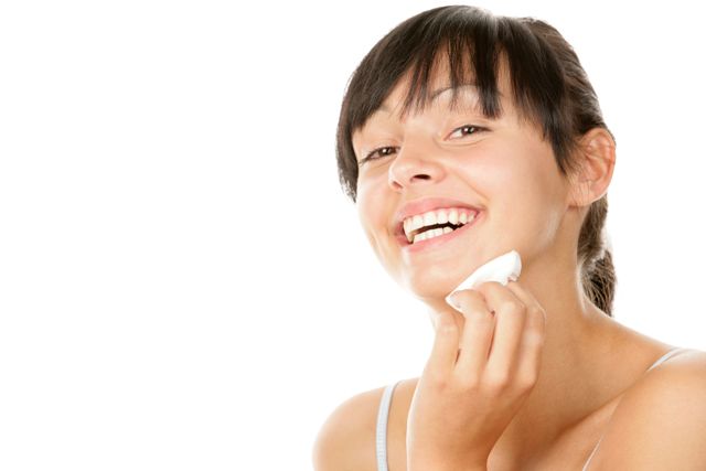 אישה מחייכת, מנקה את פניה עם פיסת כותנה.